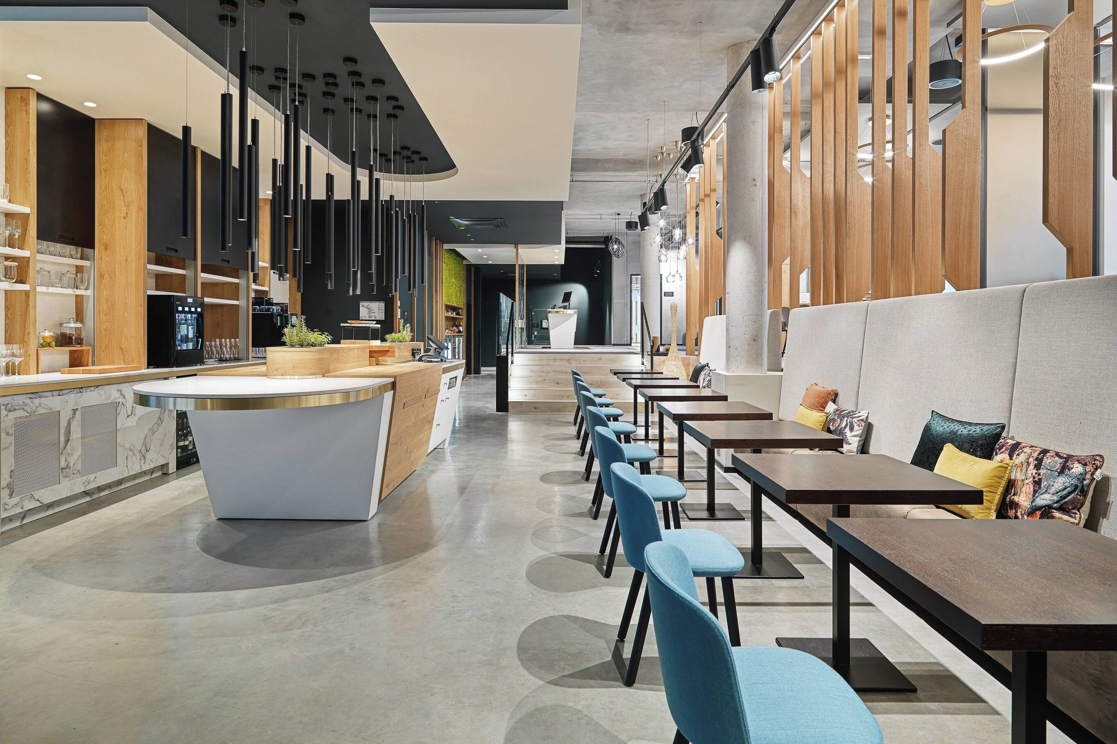 A modern restaurant interior with a central bar, seating area, and a visible kitchen.
