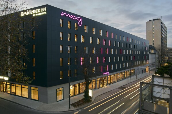 A modern hotel with a neon sign, multiple windows, and a well-lit facade.