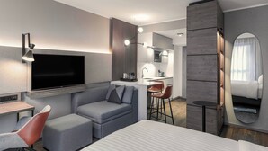 Een moderne hotelkamer met een groot bed, een bureau, een bank, een televisie, een kitchenette en een badkamer met spiegel.