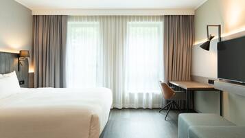 Una habitación de hotel con una cama grande, un escritorio, una silla, un televisor y cortinas.