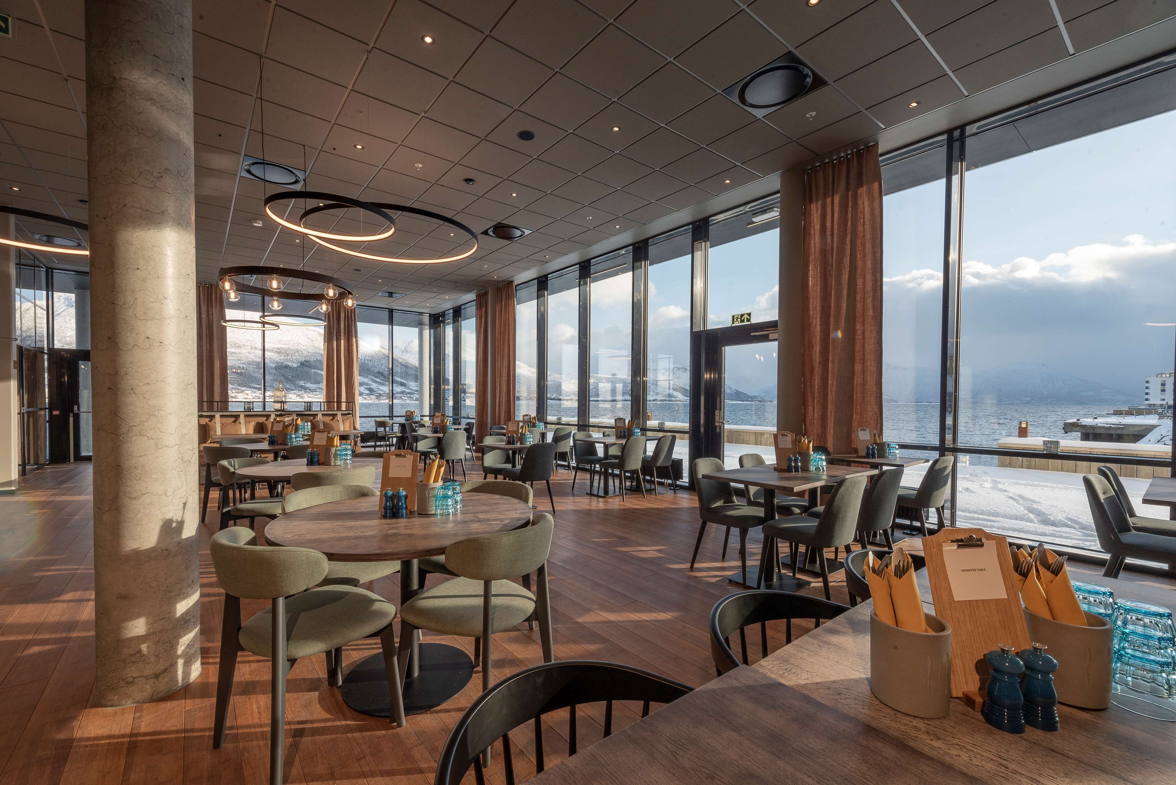Un'ampia sala da pranzo con grandi finestre, tavoli e sedie in legno.