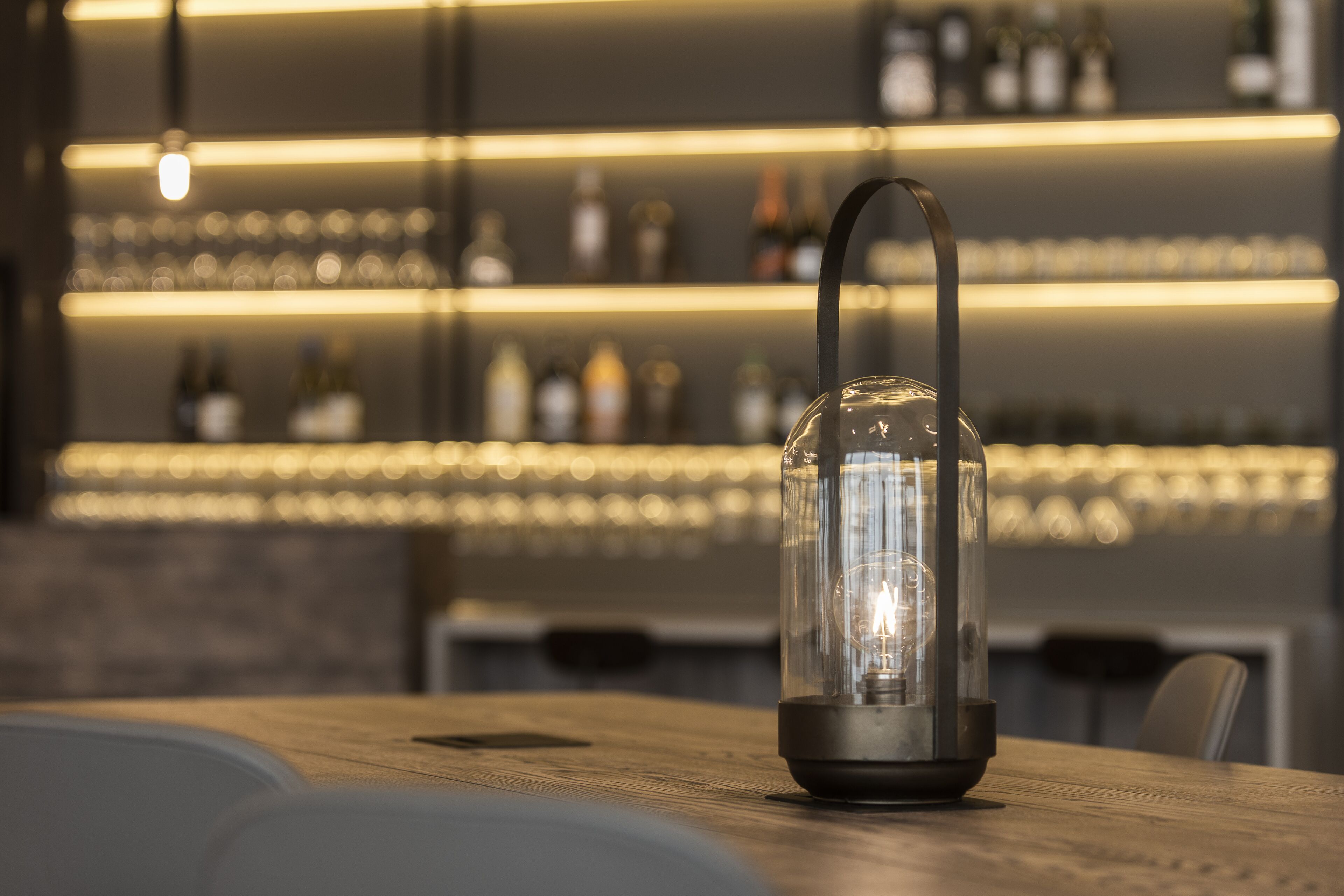 Una lanterna di vetro trasparente con manico nero su un tavolo di legno in un bar.
