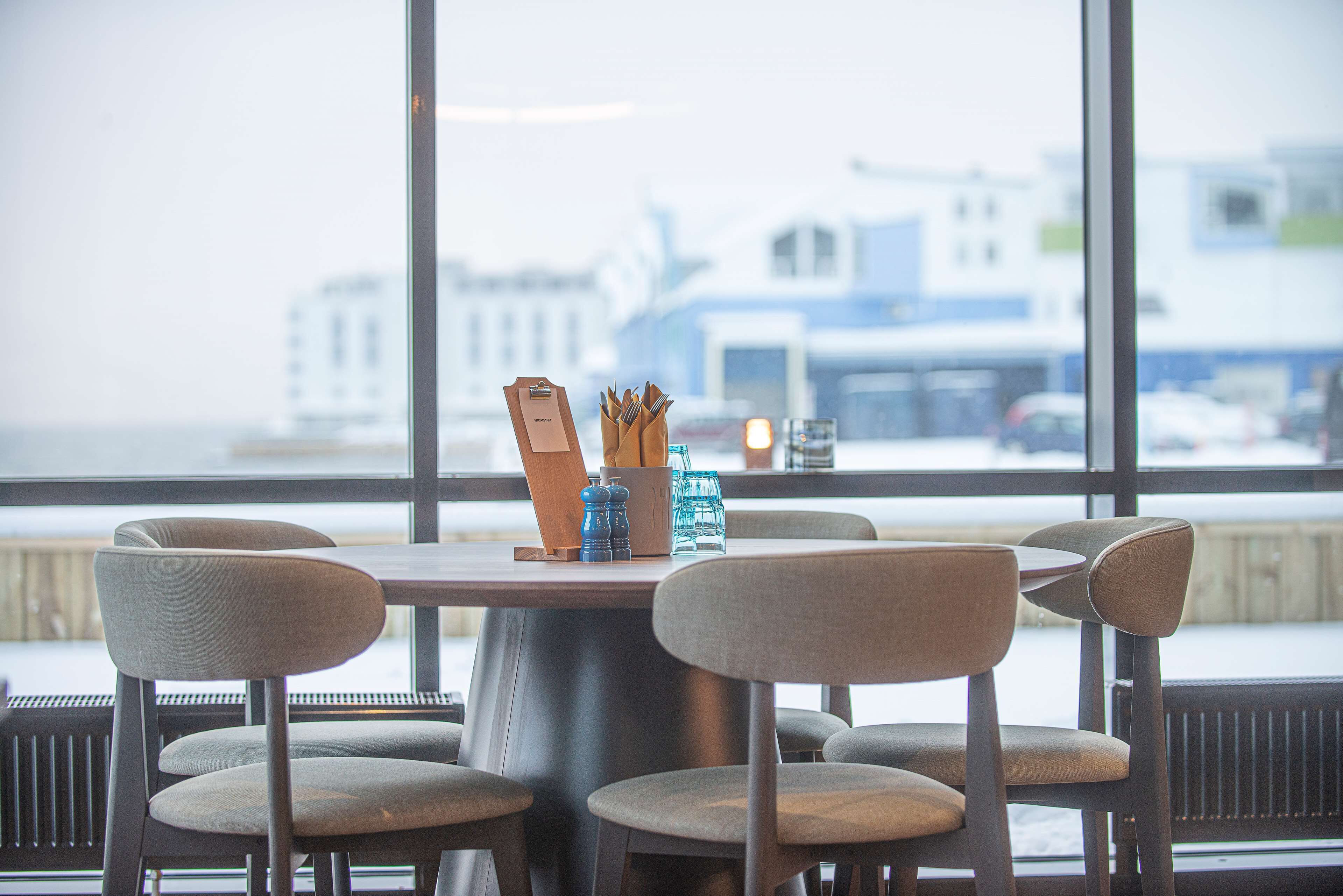 A dining area with a table and four chairs, a window with a view of buildings, and a salt and pepper shaker set on the table.