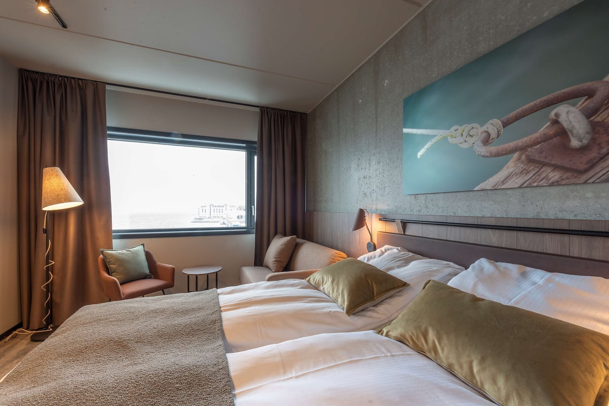 A hotel room with a large bed, a chair, a small table, and a painting on the wall.