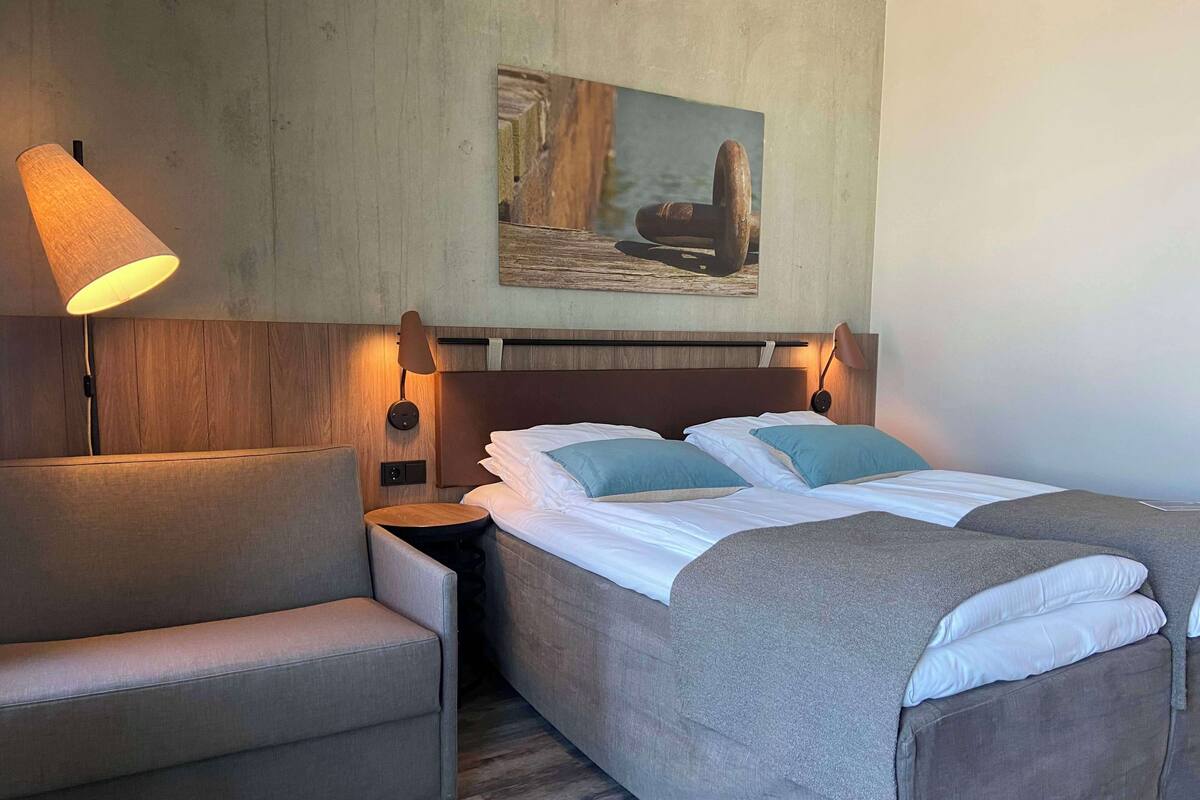 A hotel room with a bed, a chair, a nightstand, and a lamp.
