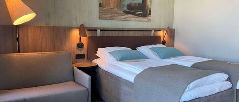 A hotel room with a bed, a chair, a nightstand, and a lamp.