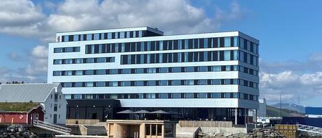 Un moderno edificio de varios pisos con techo plano, ventanas amplias y un muelle que se adentra en el agua.