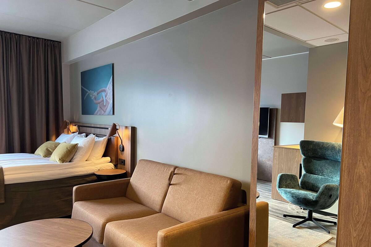 A hotel room with a bed, a sofa, a small round table, a TV, and a painting on the wall.