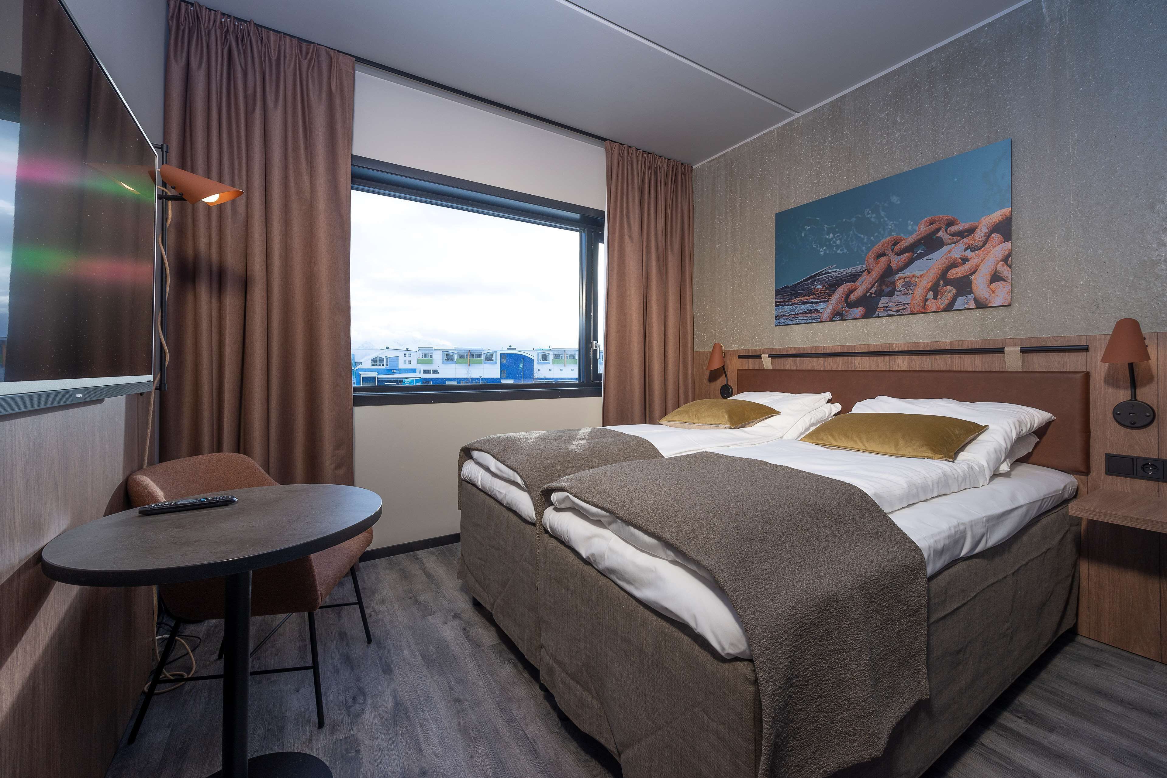 Una habitación de hotel con una cama, una mesita, una silla, una ventana con cortinas y un cuadro en la pared.