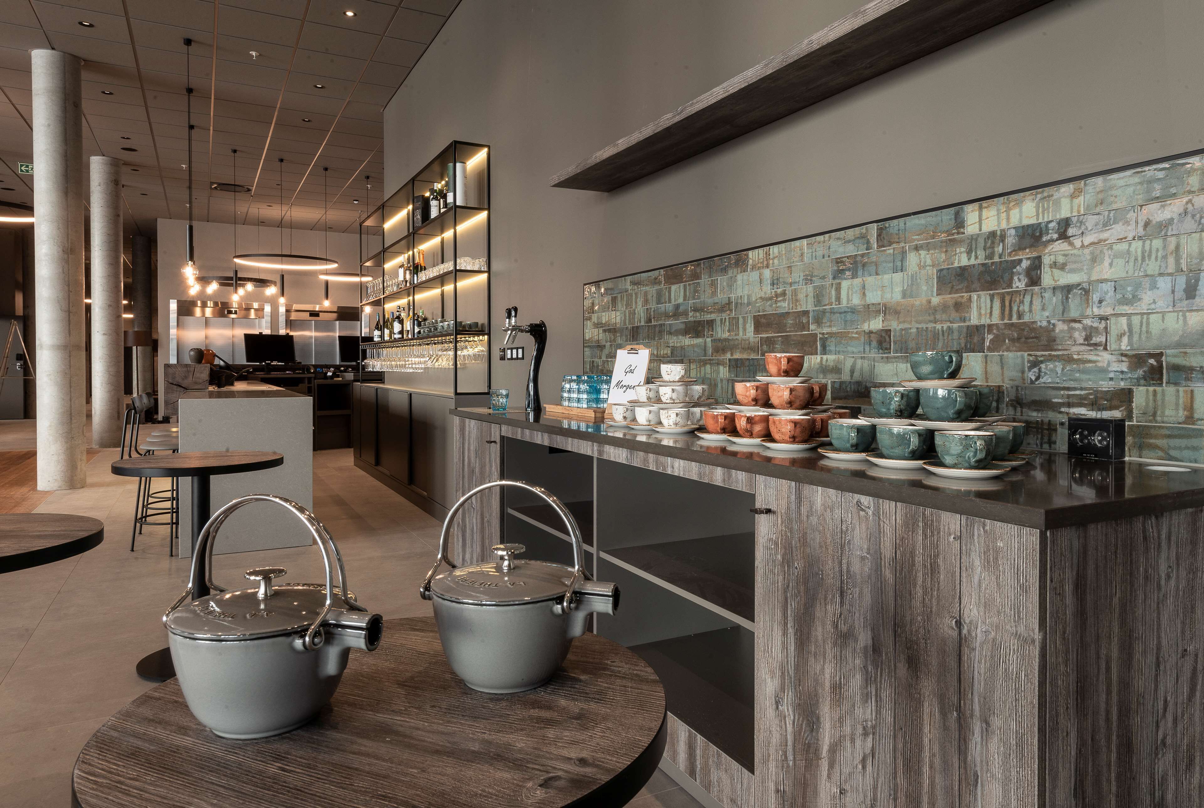 A modern kitchen area with a bar counter, kitchen appliances, and a variety of cookware and dishes displayed on the counter.