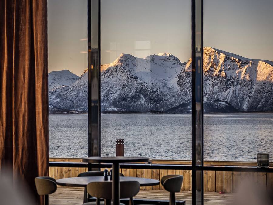 A restaurant with a view of snow-covered mountains and a body of water.