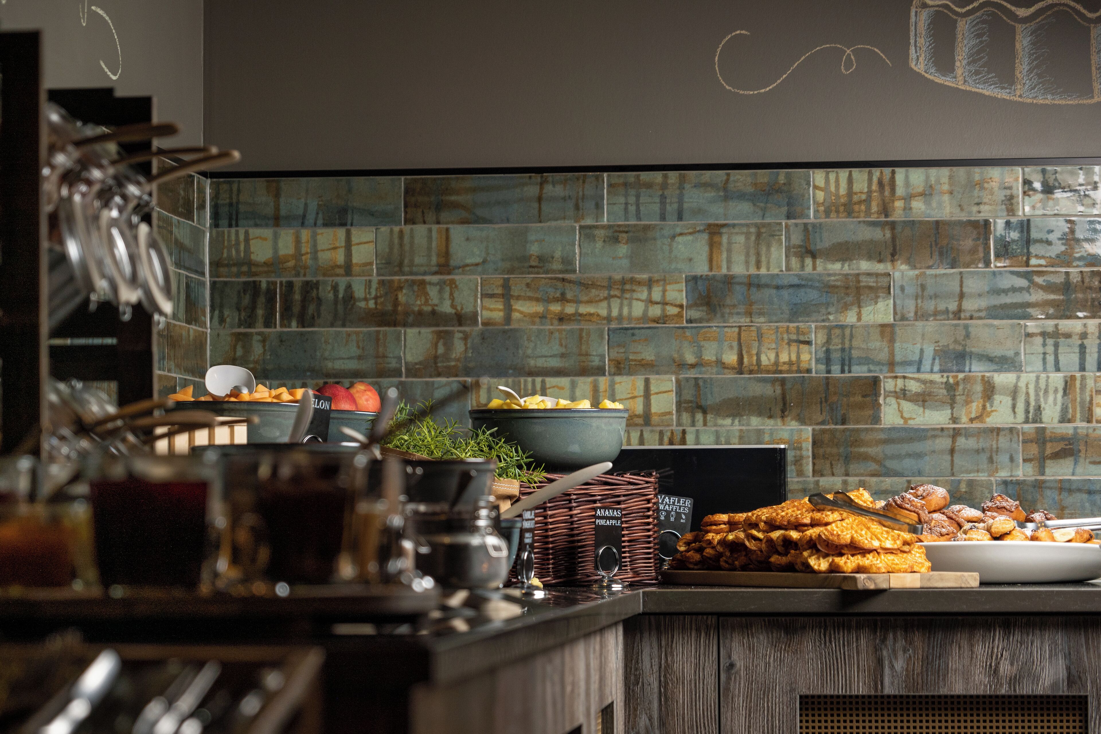 A breakfast buffet with various food items, a coffee station, and a decorative wall with a geometric pattern.