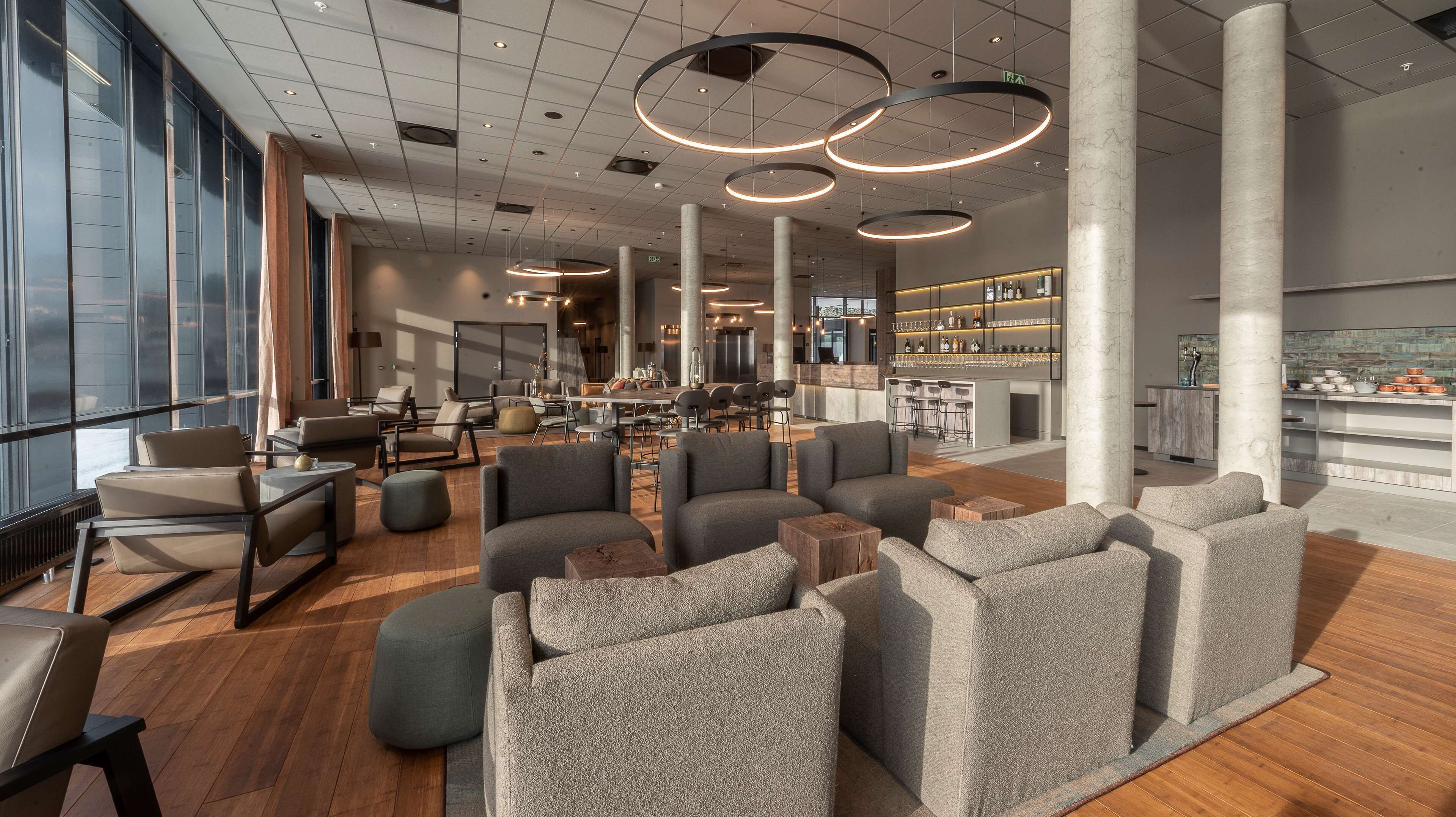 A spacious lobby with a bar area, seating arrangements, and a view through large windows.