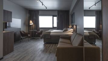 Ett modernt hotellrum med en stor säng, två fåtöljer, ett skrivbord och en tv.