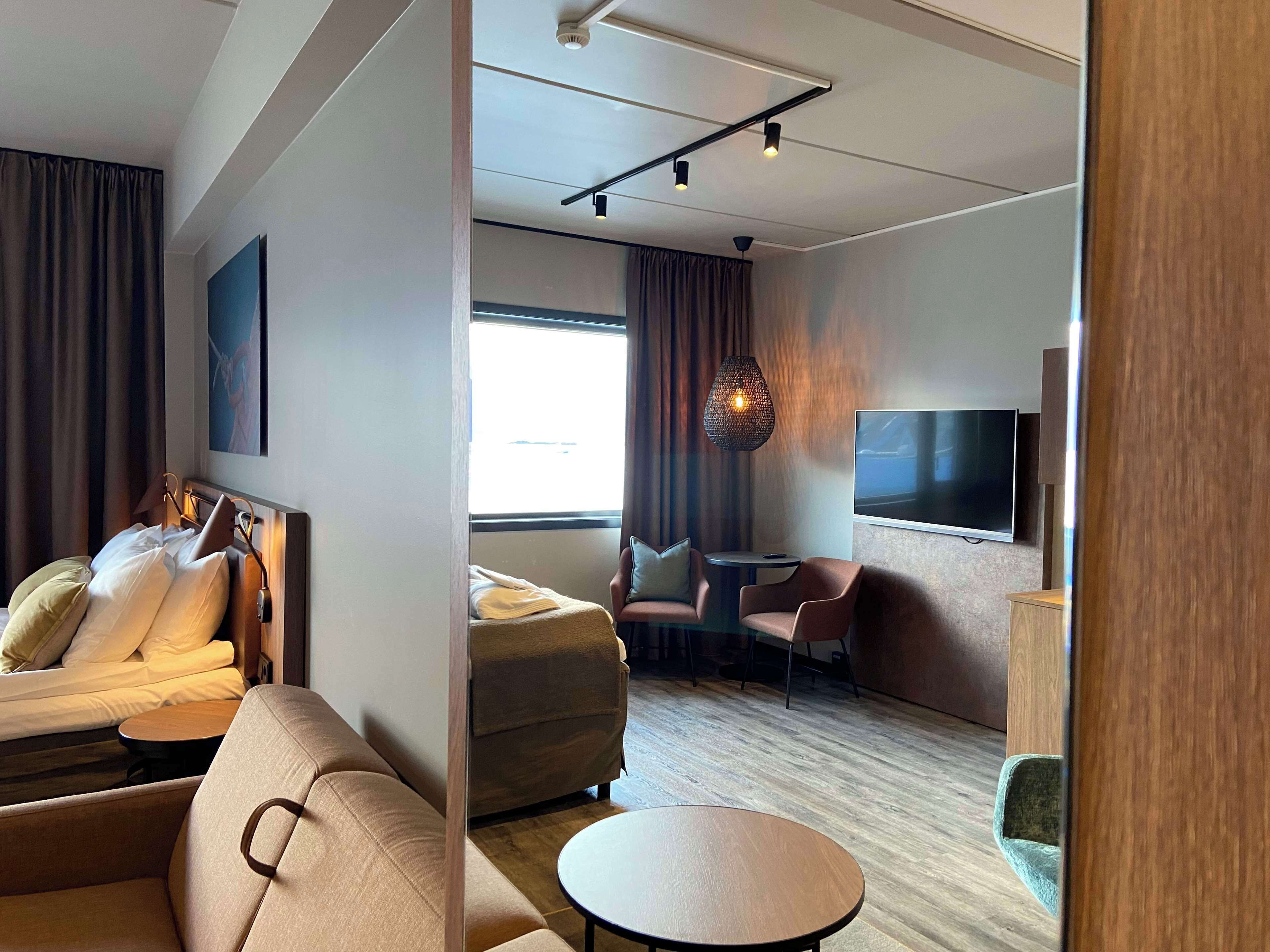 Une chambre d’hôtel moderne équipée d’un lit, d’un canapé, d’un fauteuil et d’une télévision.