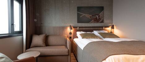 A modern hotel room with a bed, a sofa, a small table, and a painting on the wall.