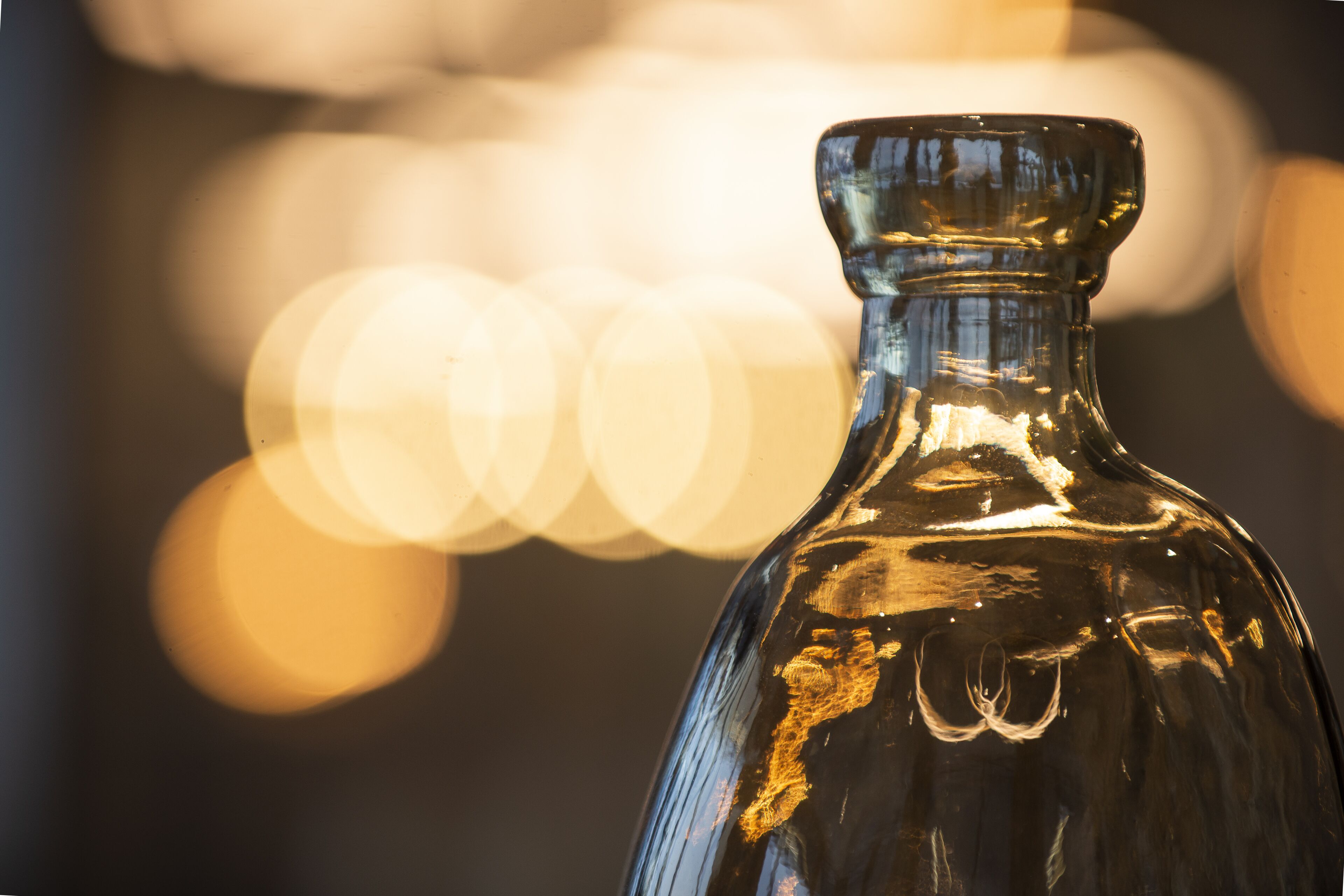 A clear view of a glass bottle with a narrow neck and a wider base, set against a blurred background with bokeh effect.