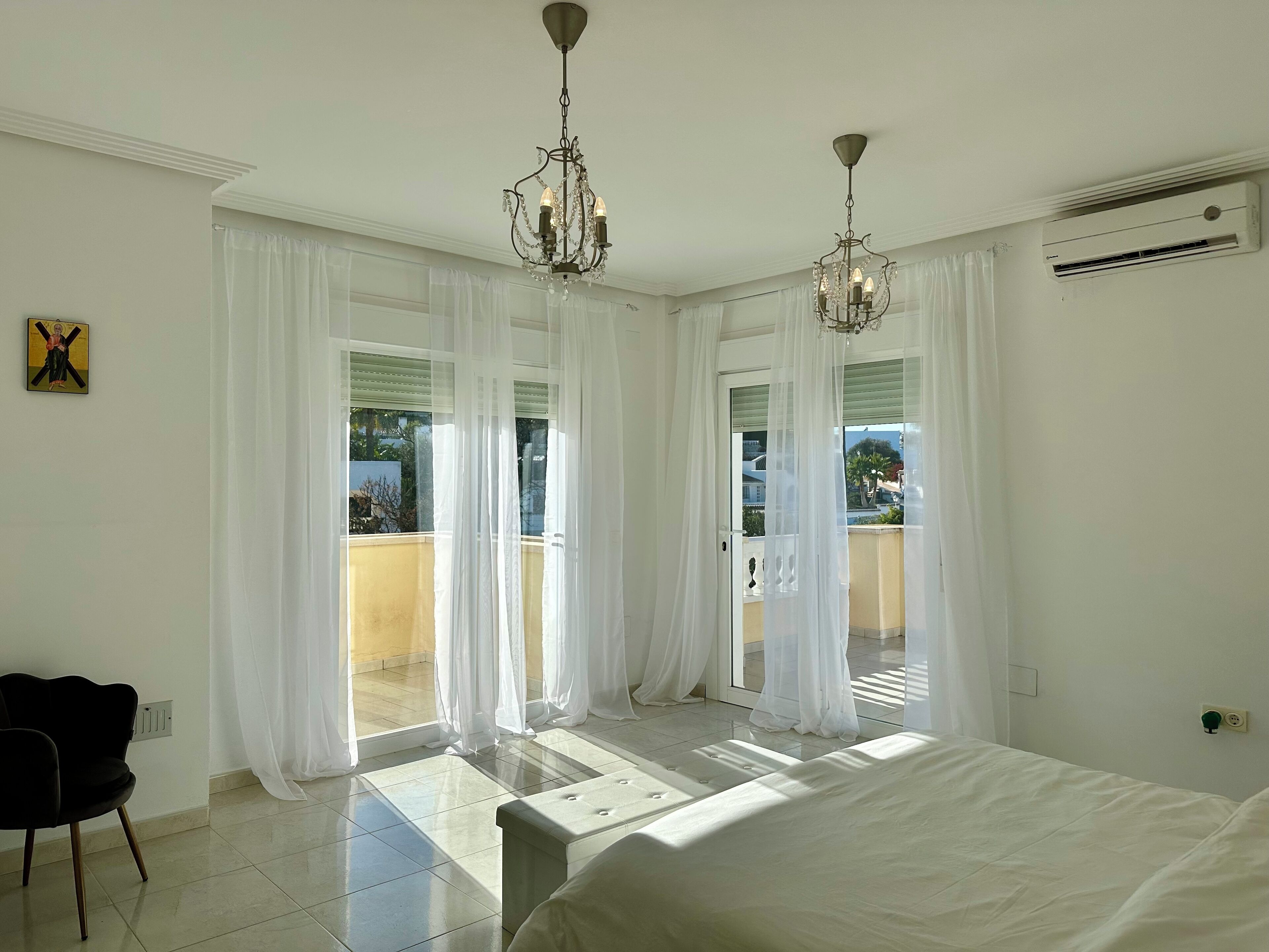 Une chambre à coucher avec un lit, une chaise, un lustre et une vue sur l’extérieur.