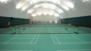 An indoor tennis court with a high, arched ceiling and green flooring.