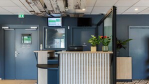 Een receptiebalie met een bureau, een computer, een plant en een bord dat parkeren en de uitgang aangeeft.