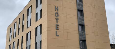A hotel building with a beige facade, multiple windows, and a prominent 'HOTEL' sign on the side.