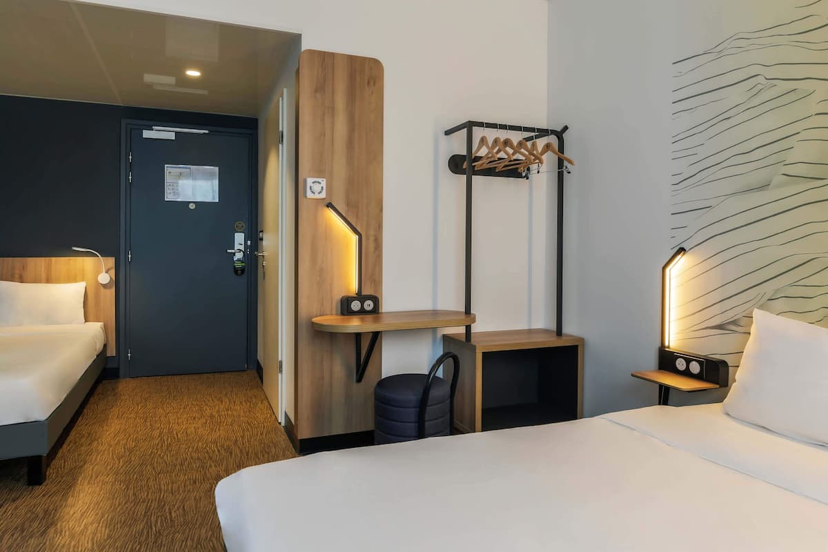 Habitación de hotel con dos camas, un escritorio, una silla, perchero y lámpara fijada a la pared.