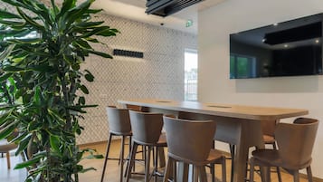 A modern bar area with a long wooden counter, several brown bar stools, and a large potted plant.