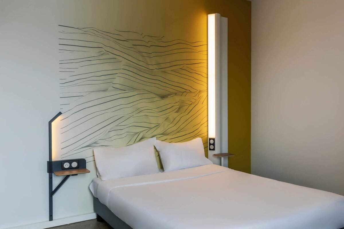 Una habitación de hotel moderna con una cama, una mesita de noche y un aplique de pared.