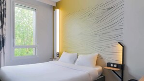 Een moderne slaapkamer met een bed, nachtkastje, wandlamp en een raam met uitzicht op bomen.