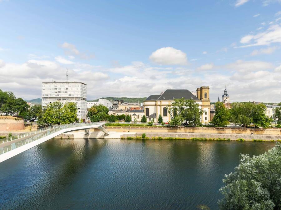 Un río con un puente peatonal, un edificio moderno y una iglesia histórica.