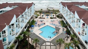 A resort with a central pool, multiple balconies, and a view of the ocean. - Seascape 2107 1 Bedroom Condo by RedAwning (Galveston)