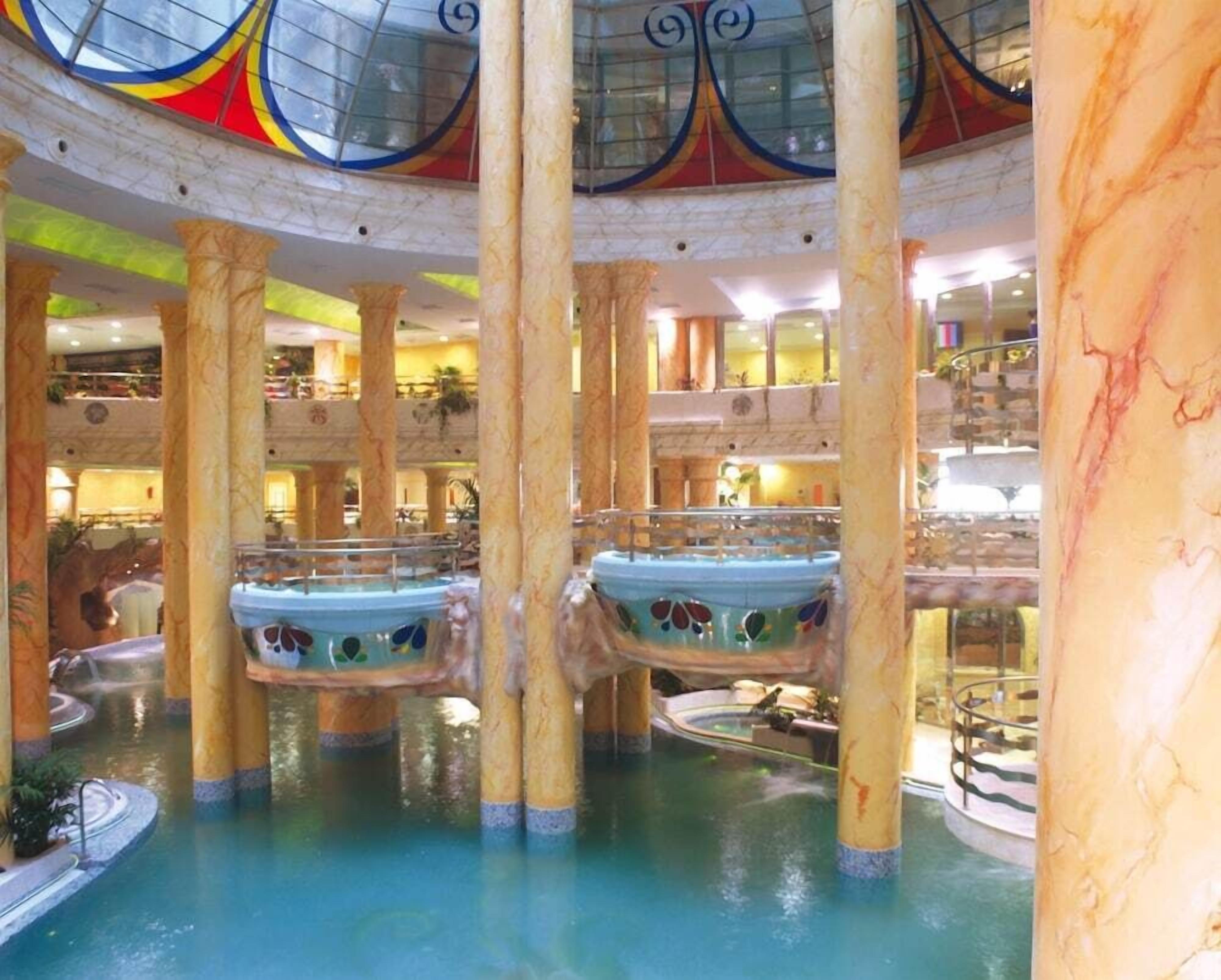 Una piscina interior de varios niveles con columnas de mármol y techo de vidrio.