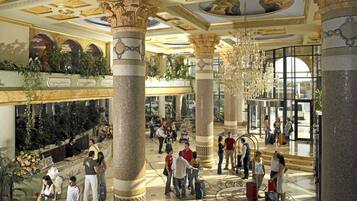 A spacious lobby with high ceilings, ornate columns, and a central chandelier.