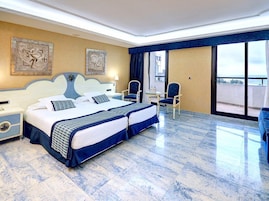 Habitación de hotel con una cama grande, dos sillas, una mesita y un balcón con vistas.