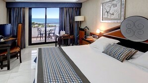 Habitación de hotel con cama, escritorio, silla, mesa, lámpara y vista al océano.