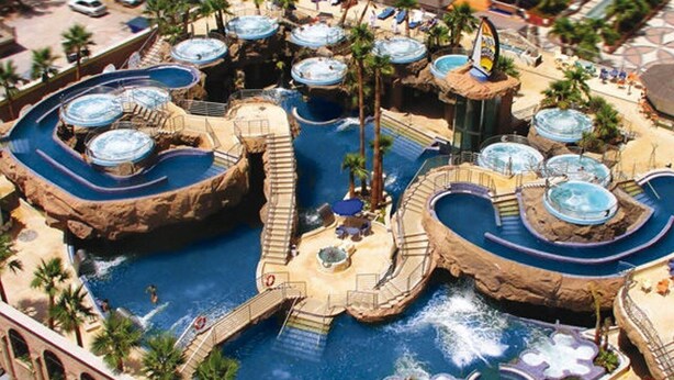 Un parque acuático con múltiples piscinas y toboganes, rodeado de palmeras y senderos.