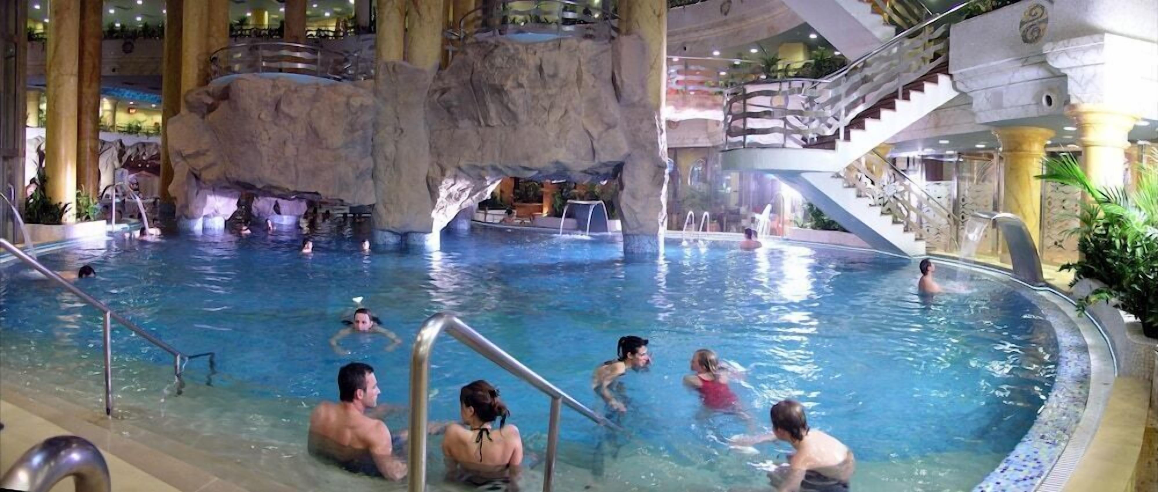 Una piscina interior con varios niveles, una formación rocosa en el centro y una escalera.