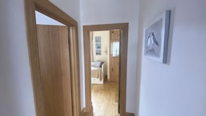 A hallway with wooden flooring leading to a bedroom with a bed and a window. - Coastal 2-bed Cottage for 4 Cellardyke, Anstruther (Anstruther)