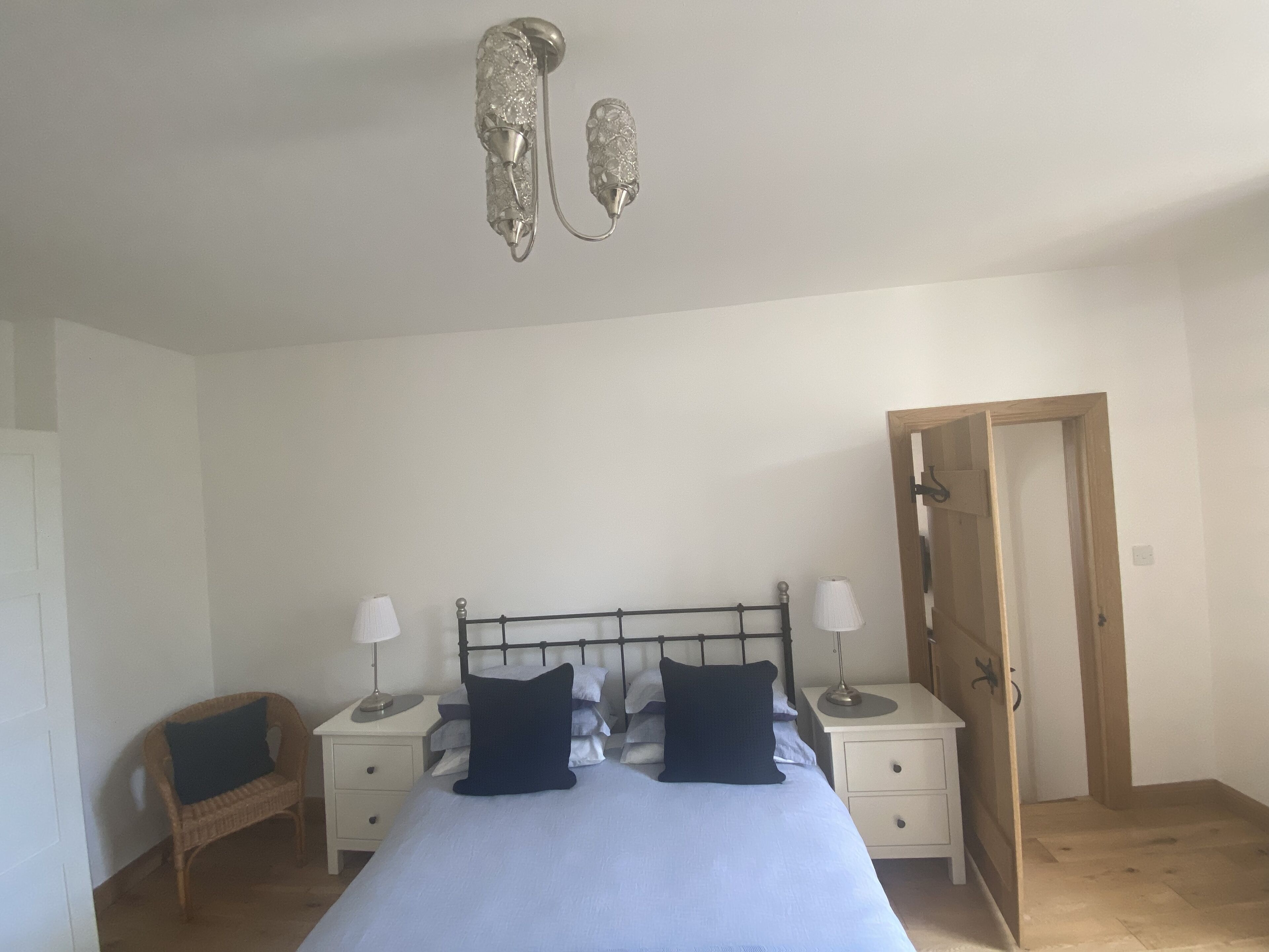 Une chambre à coucher comprenant un lit, deux tables de chevet, une chaise, une porte en bois et un luminaire au plafond.