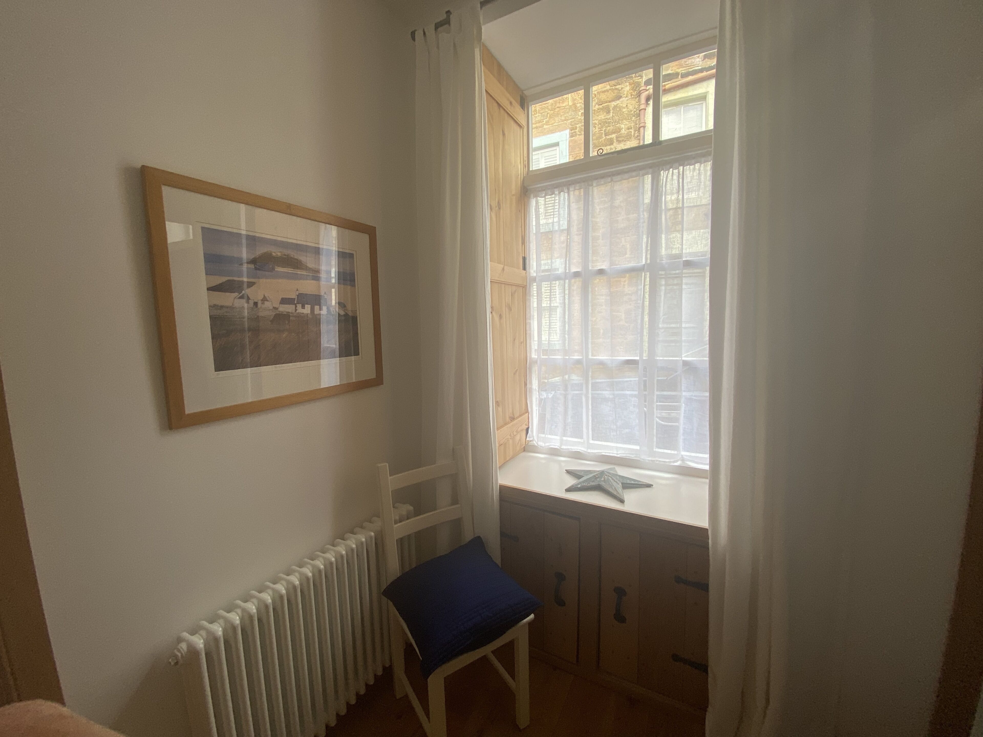 Een kamer met een witte radiator, een ingelijst kunstwerk aan de muur, een raam met uitzicht op een gebouw en een zeester decoratie op de vensterbank.