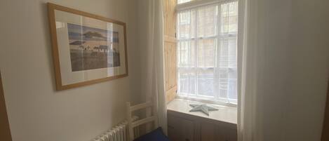 Een kamer met een witte radiator, een ingelijst kunstwerk aan de muur, een raam met uitzicht op een gebouw en een zeester decoratie op de vensterbank.