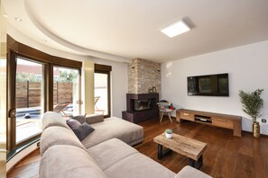 A modern living room with a stone fireplace, a large sofa, a wooden coffee table, and a TV mounted on the wall.