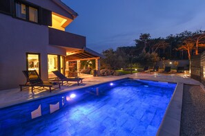 Een modern huis met een zwembad, buitenmeubilair en een goed verlicht terras.