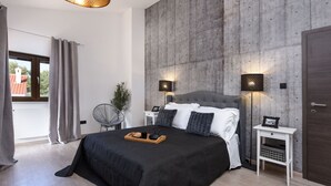 Een moderne slaapkamer met een groot bed, twee nachtkastjes, een wandlamp en uitzicht door een raam.