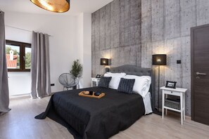Een moderne slaapkamer met een groot bed, twee nachtkastjes, een wandlamp en uitzicht door een raam.