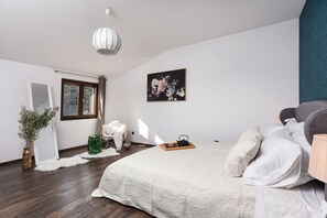 A bedroom with a large bed, a hanging light fixture, a window with curtains, a framed floral painting, and a potted plant. - Villa Trabakul ZadarVillas (Ražanac)