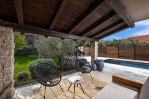 A covered patio area with stone walls, a pool, and outdoor seating.