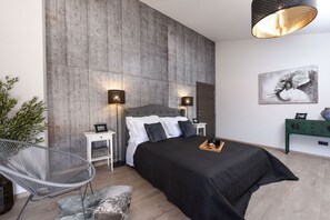 A modern bedroom with a large bed, two bedside tables, a chair, and a green console table.