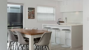 A modern kitchen with a central island, bar stools, and a dining table with chairs.