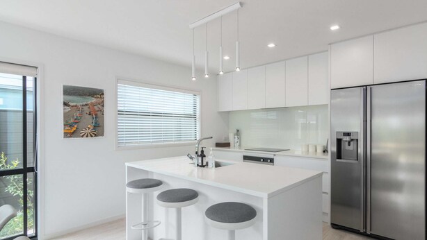 A modern kitchen with white cabinetry, a stainless steel refrigerator, and a bar area with stools.